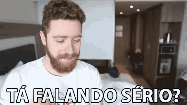 a man with a beard is sitting in front of a sign that says ta falando serio