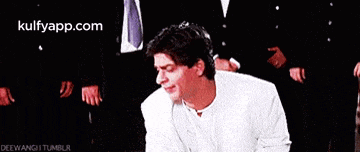 a man in a white suit and tie is kneeling down in front of a group of men in suits and ties .