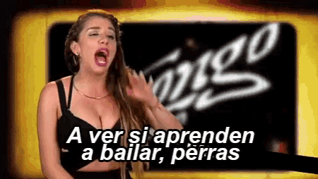 a woman in a black bra stands in front of a sign that says a ver si aprenden a bailar perras .