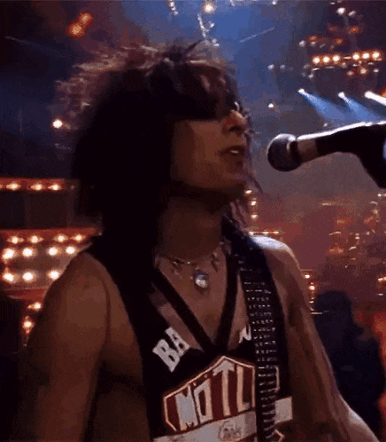 a man is singing into a microphone while wearing a shirt with the word motl on it .