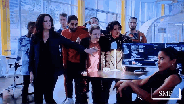 a group of people standing around a desk with a smp logo on the bottom