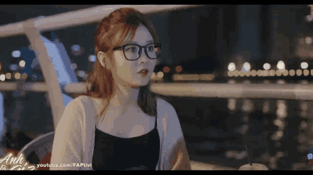 a woman wearing glasses sits at a table with a cup of coffee