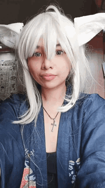 a woman wearing a white wig and a blue jacket has a cross necklace