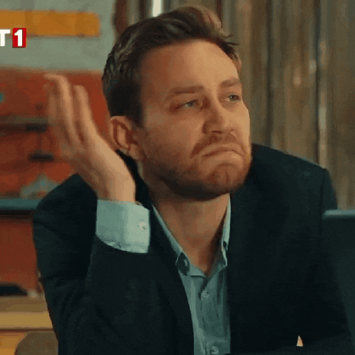 a man in a suit and blue shirt is sitting at a table with his hand on his chin ..