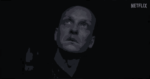 a man in a blue shirt is looking up at the sky in a dark room .
