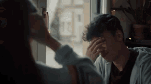 a woman is touching a man 's forehead while sitting at a table .