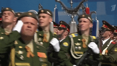 a group of men in military uniforms are marching in a parade and one of them has the letter t on his hat