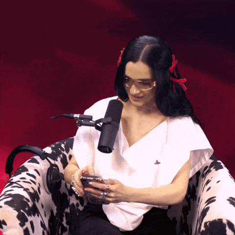 a woman wearing glasses is sitting in a chair with a microphone in front of her