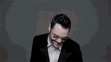 a man wearing glasses and a suit is sitting in front of a wall of cards .