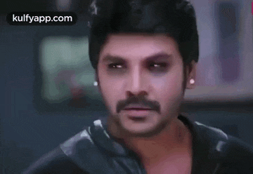 a man with a mustache and black eyes is wearing earrings and a leather jacket .