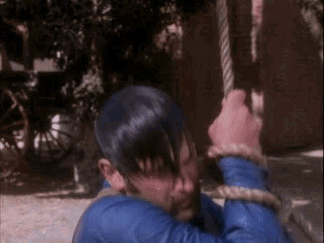 a boy in a blue shirt is playing with a rope swing
