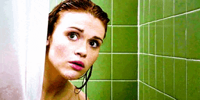 a woman is peeking out from behind a shower curtain in a shower .