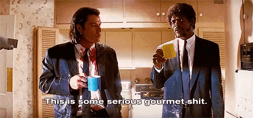 two men in suits and ties are standing in a kitchen drinking coffee and talking .