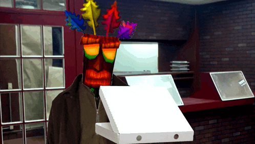 a man wearing a tiki mask holds a pizza box
