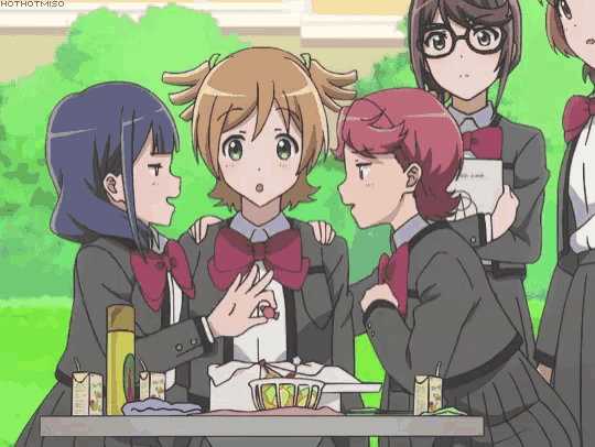 a group of anime girls are standing around a table and one of them is holding a piece of cake