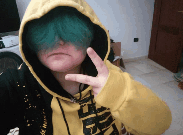 a person with green hair wearing a yellow hoodie that says " de mun " on it