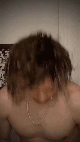 a man without a shirt is wearing a chain around his neck and his hair is flying in the air .