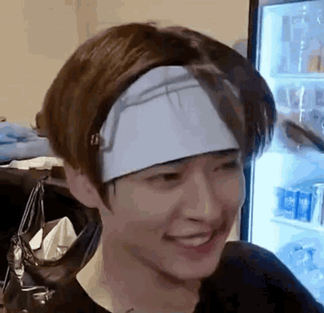 a young man wearing a headband is smiling in front of a fridge .
