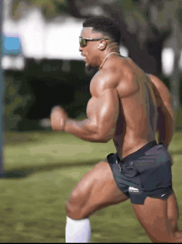 a shirtless muscular man wearing sunglasses and shorts is running