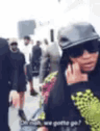 a woman wearing sunglasses and a hat is talking on a cell phone in a crowd of people .