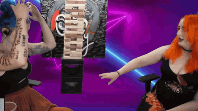 two women are playing a game of jenga and one has a tattoo on her arm that says " i love you "