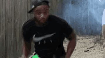 a man wearing a black nike shirt and a hat is standing in front of a fence .