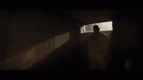 a man is standing in a dark room looking out a window .