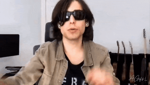a man wearing sunglasses and a jacket is sitting in a chair in front of a computer .