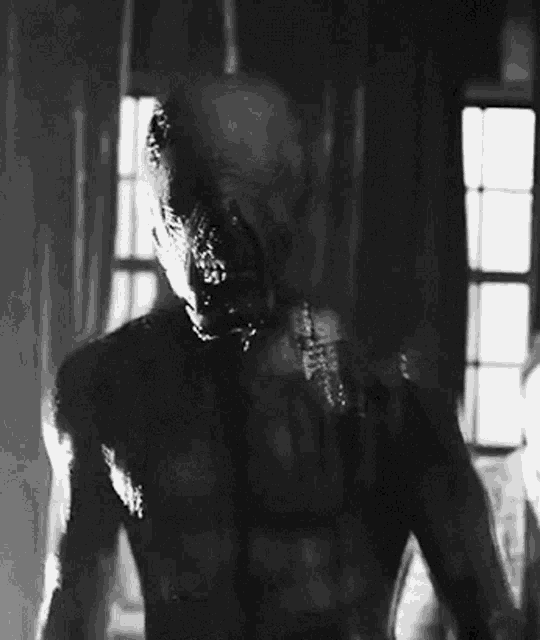 a black and white photo of a man with a bandaged head standing in front of a window .