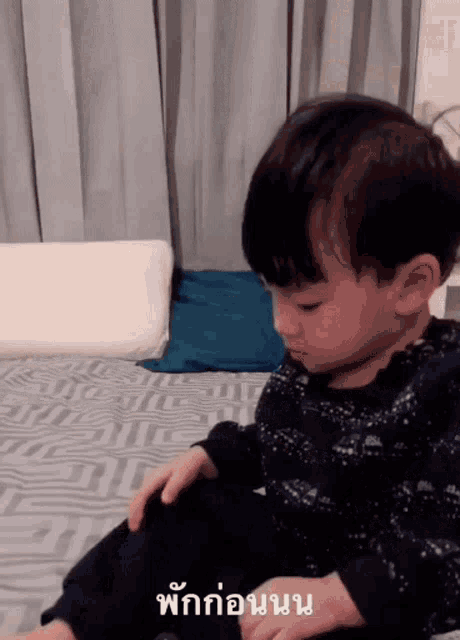 a little boy is sitting on a bed with a foreign language written on the bottom
