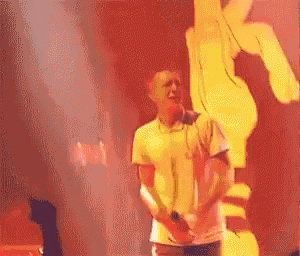 a man is singing into a microphone on a stage in front of a large hand
