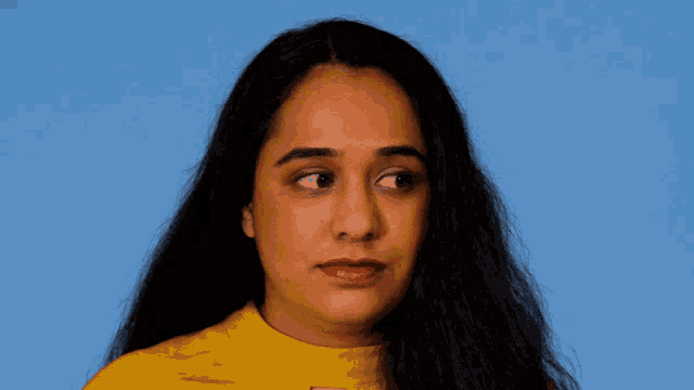 a woman with long dark hair wearing a yellow shirt and red lipstick