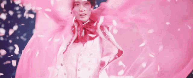 a woman is wearing a pink cape with petals falling around her