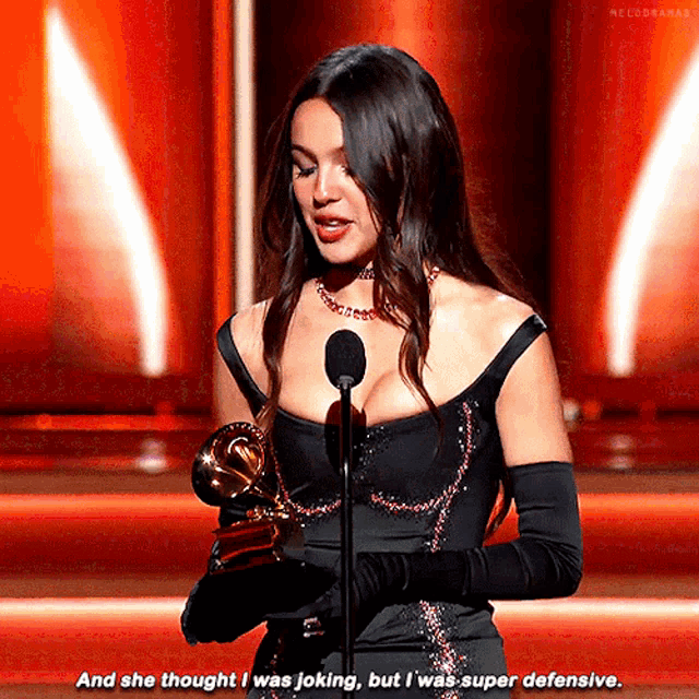 a woman in a black dress is speaking into a microphone while holding a trophy ..
