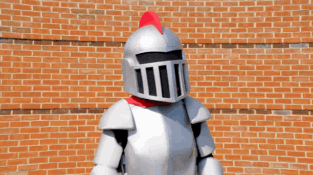 a knight mascot giving two thumbs up in front of a red brick wall