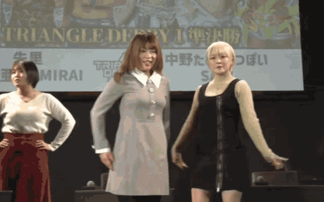 three women stand in front of a triangle derby sign