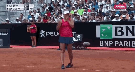 a woman stands on a tennis court in front of a bnp pariba sign