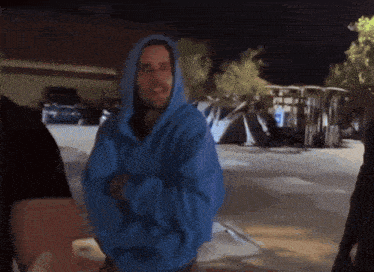 a man wearing a blue hoodie is standing in a parking lot