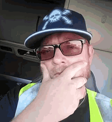 a man wearing a hat and sunglasses is covering his mouth