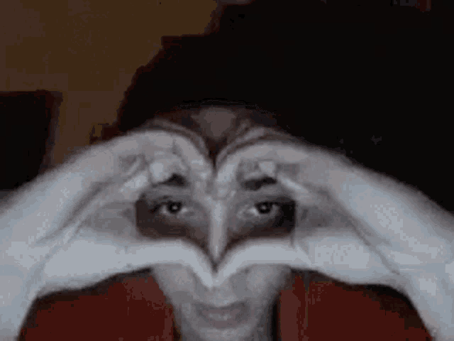 a woman is making a heart shape with her hands over her eyes .