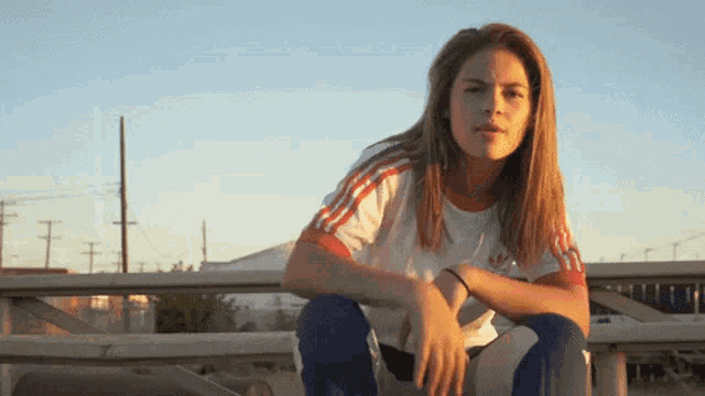 a woman wearing an adidas shirt sits on a fence