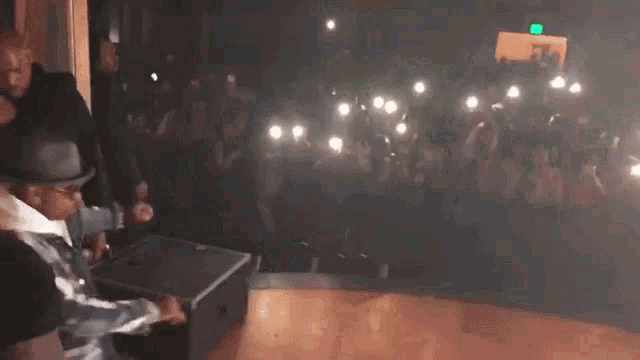 a man in a hat is standing on a stage with a crowd behind him