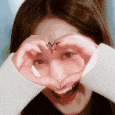 a woman is making a heart with her hands in front of her face .