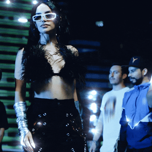 a woman wearing sunglasses and a feathered top stands in front of a group of people