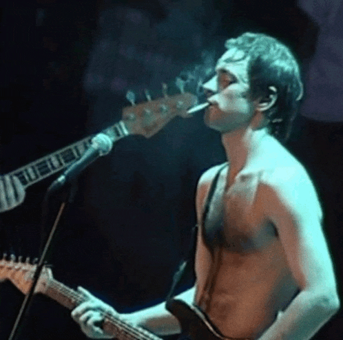 a man smoking a cigarette while playing a guitar and singing into a microphone