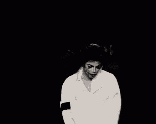 a black and white photo of a man in a white shirt dancing in a dark room .