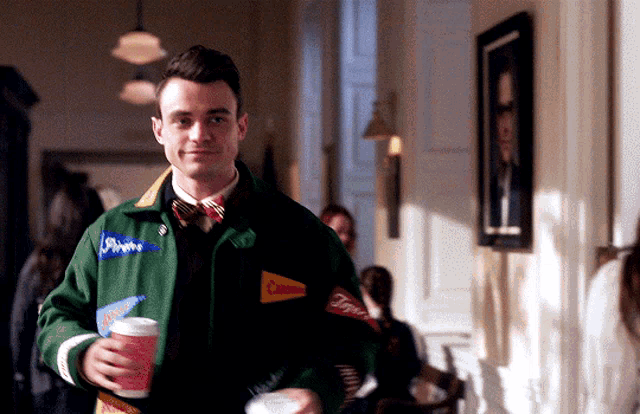a man in a green jacket holds a cup of coffee and a flag that says columbia