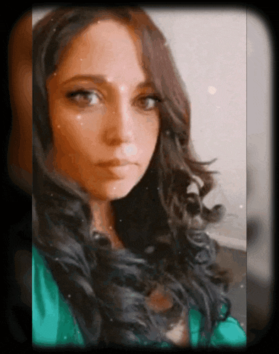 a woman with long dark hair and a green shirt looks at the camera