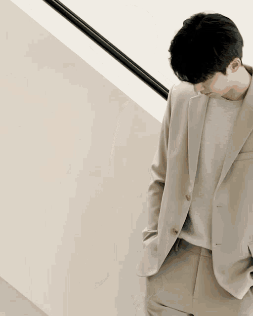 a man in a tan suit is leaning against a white wall
