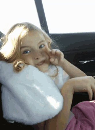 a little girl sitting in a car with a white pillow on her neck
